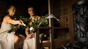 Woman pouring water on stones in Finnish sauna